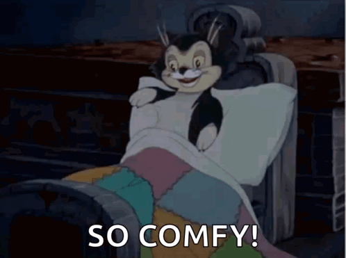 A Cartoon Cat Is Laying In A Bed With The Words `` So Comfy '' Written Below It . GIF