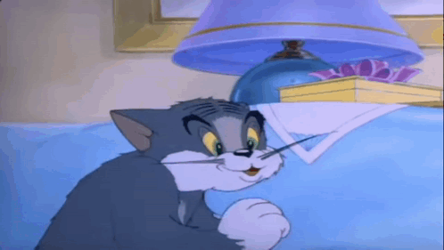 A Cartoon Cat Is Sitting On A Bed Under A Lamp GIF