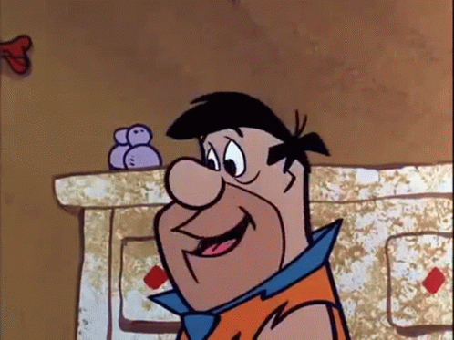 A Cartoon Character From The Flintstones Is Smiling While Standing In Front Of A Fireplace . GIF