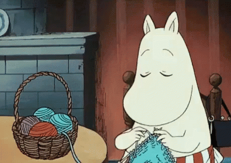 A Cartoon Character Is Knitting A Sweater In Front Of A Basket Of Yarn . GIF