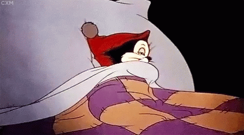 A Cartoon Character Is Laying In Bed With A Purple Blanket GIF