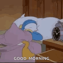 A Cartoon Character Is Sleeping On A Bed Next To An Alarm Clock And Says `` Good Morning '' . GIF