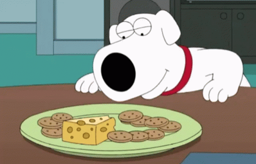A Cartoon Dog Laying On A Table Looking At A Plate Of Cheese And Cookies GIF