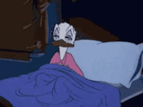 A Cartoon Duck Is Laying In Bed With A Blue Blanket GIF