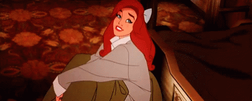 A Cartoon Girl With Red Hair Is Sitting On A Couch And Smiling . GIF