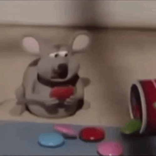 A Cartoon Mouse Is Sitting On A Table Eating A Heart Shaped Candy . GIF