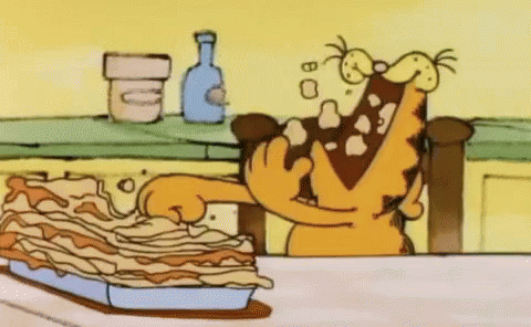 A Cartoon Of Garfield Eating A Lasagna On A Table . GIF