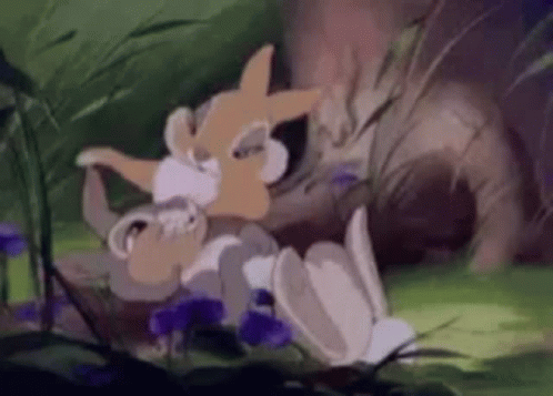 A Cartoon Rabbit Is Laying On The Ground In The Grass . GIF