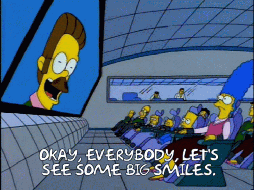 A Cartoon Says Okay Everybody Let 'S See Some Big Smiles In Front Of A Large Screen GIF