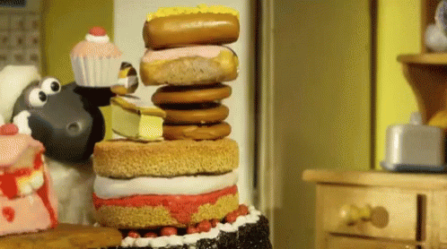 A Cartoon Sheep Is Standing Next To A Stack Of Cake And Donuts GIF