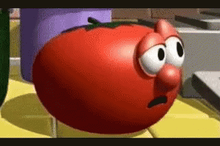A Cartoon Tomato With Big Eyes And A Big Nose Is Sitting On A Table . GIF
