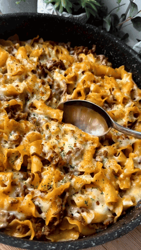 A Casserole Dish With Noodles And Cheese And A Spoon GIF