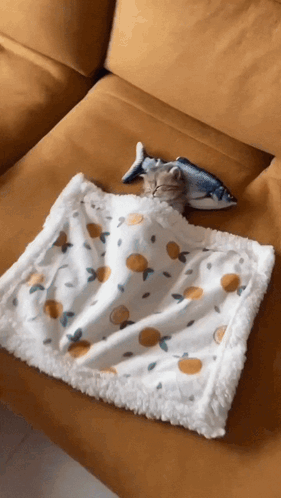A Cat Is Sleeping On A Yellow Couch Under A Blanket With Lemons On It GIF