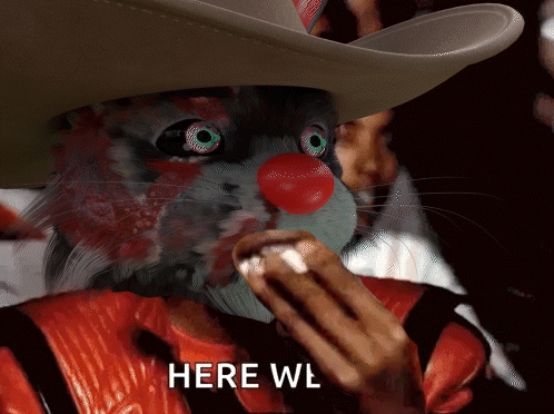 A Cat Wearing A Cowboy Hat And A Red Nose Eating A Hot Dog With The Words Here Wl Below It GIF