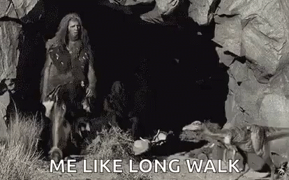 A Caveman Is Walking Through A Cave With A Dog . GIF
