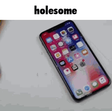 A Cell Phone With A Cracked Screen Is Sitting On A Table With The Words Holesome Above It . GIF