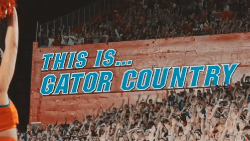 A Cheerleader In Front Of A Sign That Says This Is Gator Country GIF