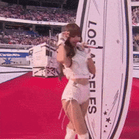 A Cheerleader Is Singing Into A Microphone In Front Of A Los Angeles Sign GIF
