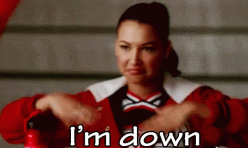 A Cheerleader Is Sitting At A Table With Her Hands Folded And The Words `` I 'M Down '' Written Below Her . GIF