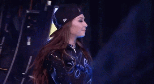 A Cheerleader Wearing A Black Hat And A Blue Shirt Is Standing On A Stage . GIF