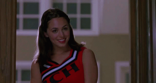 A Cheerleader Wearing A Red , Black And White Top With The Word Cheer On It Is Smiling . GIF