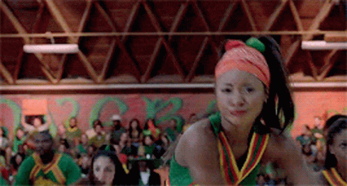 A Cheerleader Wearing An Orange Headband Is Dancing In Front Of A Crowd In A Gym . GIF