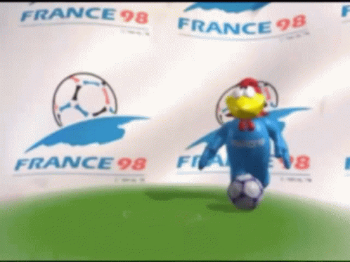 A Chicken Mascot Is Kicking A Soccer Ball In Front Of A Banner That Says France 98 GIF