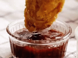 A Chicken Nugget Is Being Dipped Into A Small Bowl Of Sauce . GIF