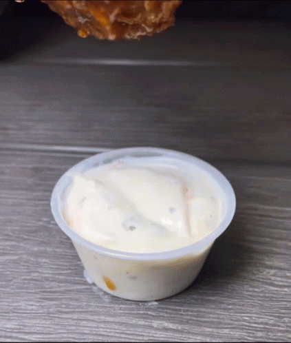 A Chicken Wing Is Being Dipped Into A Small Cup Of Ranch Dressing GIF