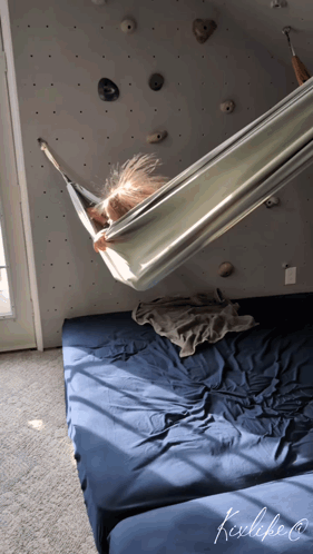 A Child Is Laying In A Hammock In Front Of A Wall With Rocks GIF