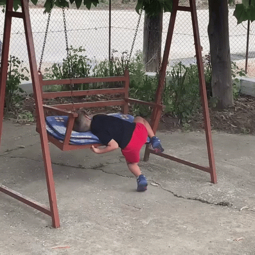 A Child Is Laying On A Wooden Swing With A Blue And White Blanket GIF