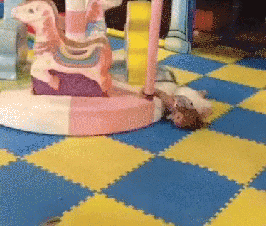 A Child Is Laying On The Floor In Front Of A Colorful Carousel GIF