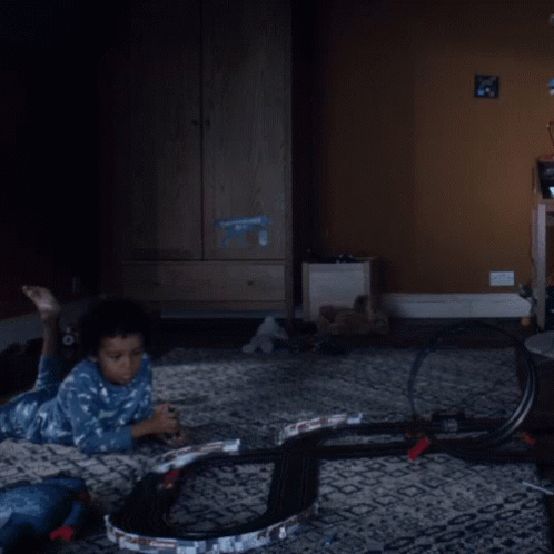 A Child Is Laying On The Floor Playing With A Toy Track GIF