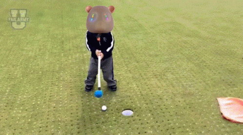 A Child Is Laying On The Grass With A Flag In Front Of A Golf Ball GIF