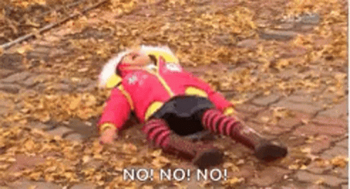 a child is laying on the ground covered in leaves and saying no ! no ! no !