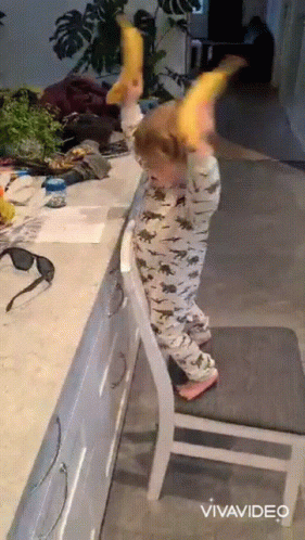 A Child Is Standing On A Chair And Holding A Banana In His Hands GIF