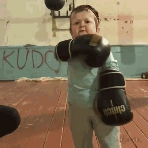 A Child Wearing Boxing Gloves With The Word Kudo On The Wall Behind Him GIF
