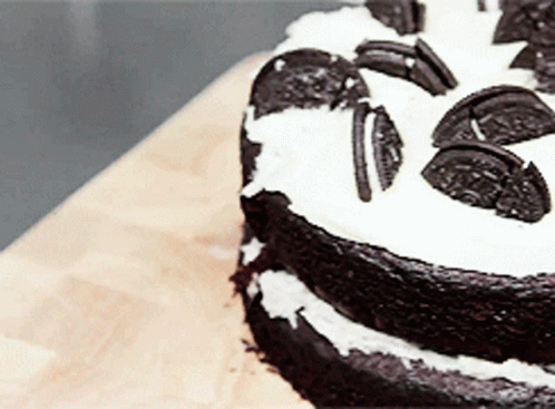 A Chocolate Cake With Oreos On Top Is On A Wooden Table GIF