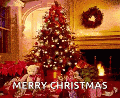 A Christmas Tree Is Sitting In Front Of A Fireplace In A Living Room With Gifts Underneath It . GIF