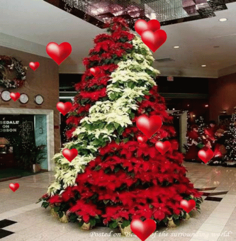 A Christmas Tree With Red And White Flowers And Hearts Surrounding It GIF