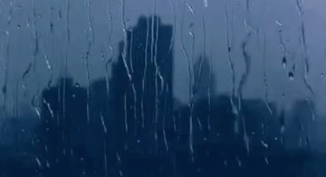 A City Skyline Is Reflected In A Window With Rain Drops On It . GIF