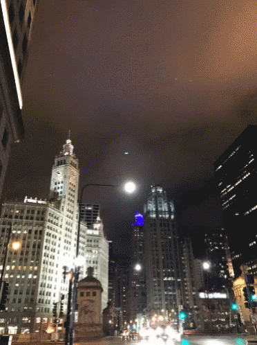 A City Street At Night With A Clock Tower And A Building That Says ' Bank Of America ' On It GIF