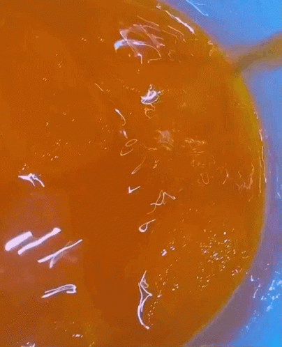 A Close Up Of A Bowl Of Orange Liquid With A Yellow Spoon In It GIF
