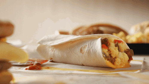 A Close Up Of A Burrito On A Table With Chips GIF