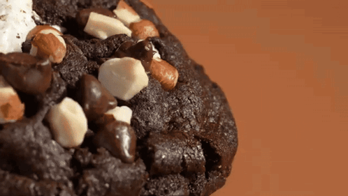 A Close Up Of A Chocolate Cookie With White Chocolate Chips And Nuts GIF
