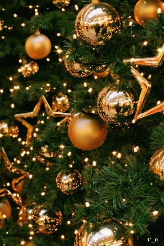 A Close Up Of A Christmas Tree With Gold Ornaments And Lights GIF
