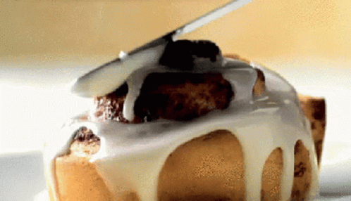A Close Up Of A Cinnamon Roll With White Frosting On It GIF