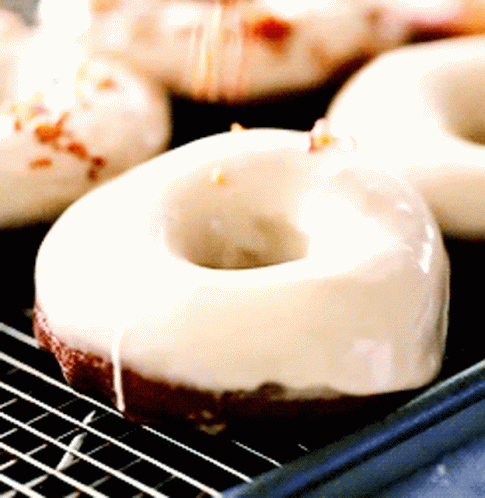 A Close Up Of A Donut With White Frosting On A Cooling Rack GIF