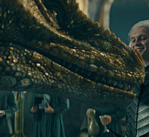 A Close Up Of A Dragon 'S Head With A Woman Holding A Glass Of Wine GIF