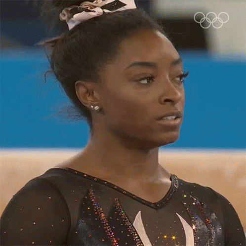 A Close Up Of A Female Gymnast 'S Face With The Olympic Rings Behind Her GIF